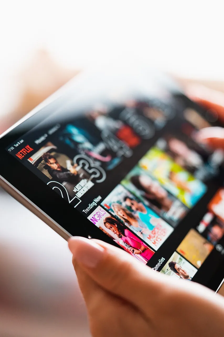 Close-up van een hand die een tablet vasthoudt met het Netflix selectiescherm zichtbaar.