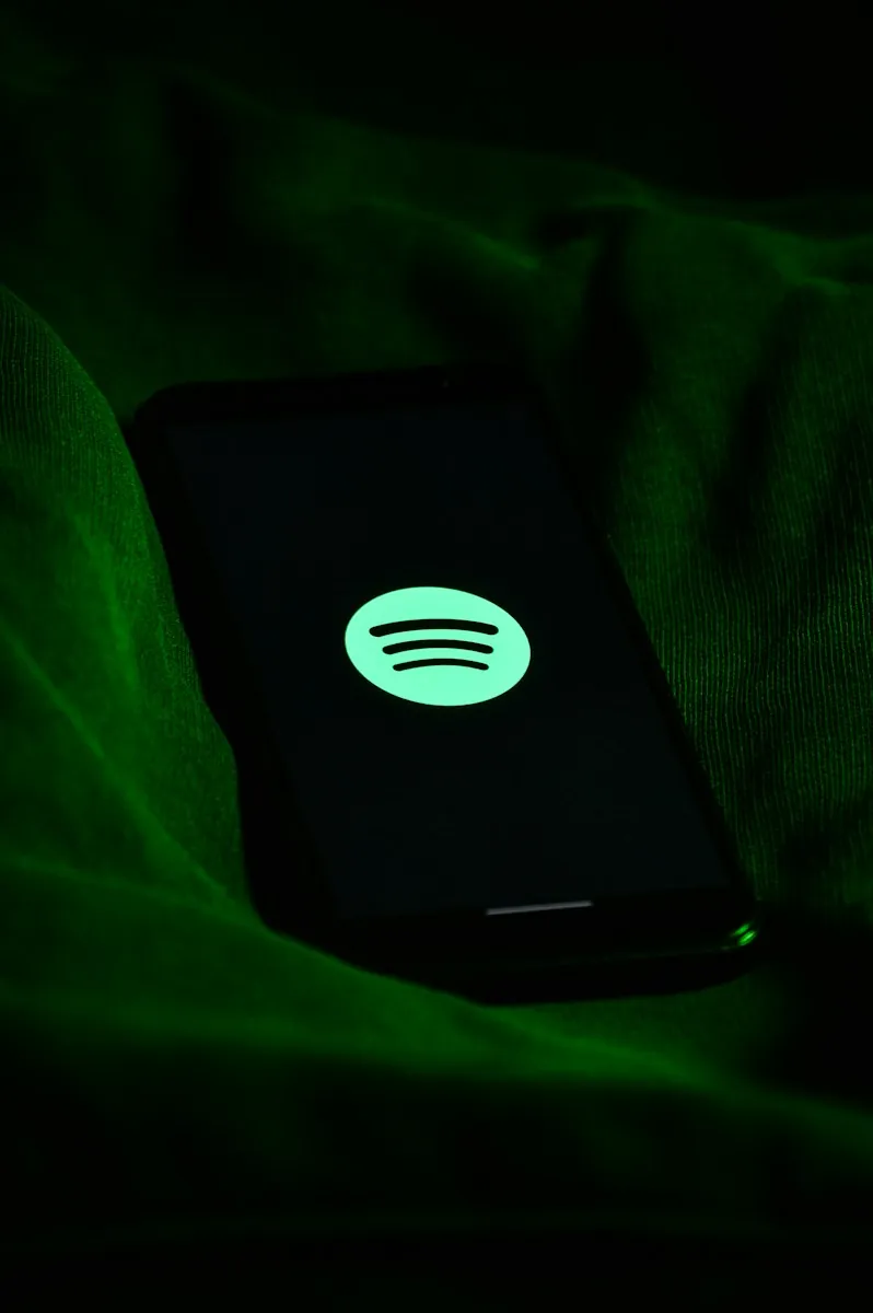Een smartphone liggend op een stof met een groene verlichting, met het Spotify-logo zichtbaar op het scherm